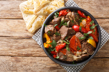 Delicious buglama meat stewed with vegetables and herbs in its own juice close-up in a bowl on a wooden table. horizontal top view from above