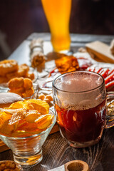 Glass of beer on bar counter. Jugs, mugs, pints of brew beverage, ale, cider on wooden table in pub, bar. Backlit dark showcase with craft beer bottles in brewery. French fries fried potatoes snack