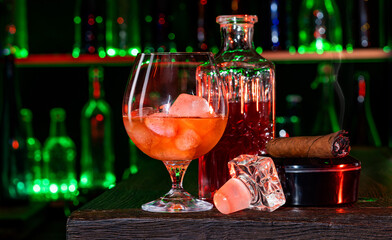 Cigar, elegant glass of brandy on the bar counter. Alcoholic drinks, cognac, whiskey, port, brandy, rum, scotch, bourbon. Vintage wooden table in a pub at night