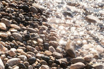Sun reflection on the wet pebbles and moving wave, crystal sea water.