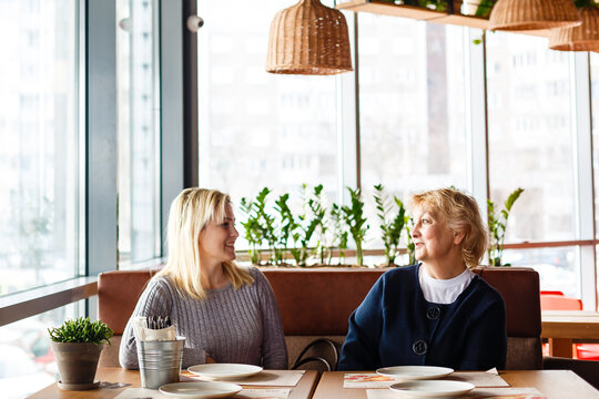 Two Happy Women Talking In Cafe. Aged Woman And Her Adult Daughter Drinking Coffee At Cafe. Mothers Day.