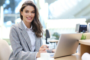 Portrait of a cheerful young businesswoman sitting at the table in office and looking at camera.