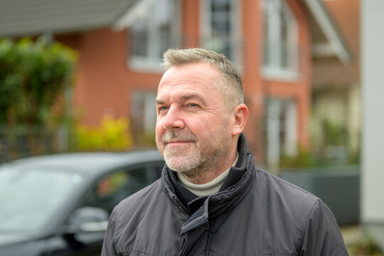 Pensive Man Standing Outside An Urban House With Car