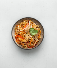 Stir fry noodles in ceramic bowl on white background, top view
