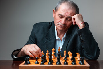 Portrait of professional chess player holding his head, thinking of strategy while moving pawn. Classical formal suit and hat, vintage look. Intellectual man playing a leisure chess match match.