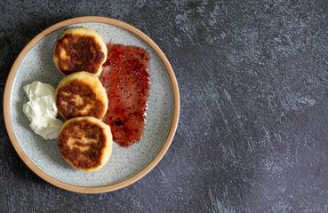 fried cottage cheese pancakes with sour cream on dark background top view
