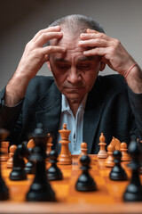 Portrait of focused man concentrated on chess match, holding head with his hands. 
Classical formal suit, vintage look. Professional challenge, thinking of strategy, analysing board.