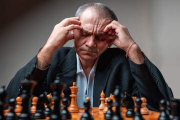 Portrait of thoughtful man concentrated on chess match, holding head with his hands thinking of his next move. 
Classical formal suit, vintage look. Professional strategy competition.