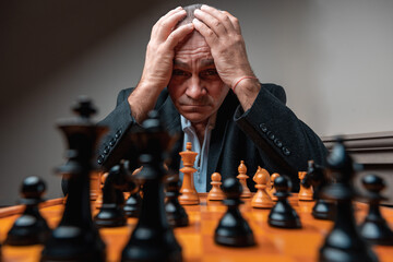 Portrait of focused man concentrated on opponent on chess match, holding head with his hands. 
Classical formal suit, vintage look. Professional challenge, thinking of strategy, reading player.