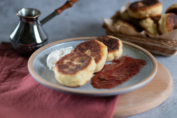 fried cottage cheese pancakesonand jezve on a wooden board with red textiles