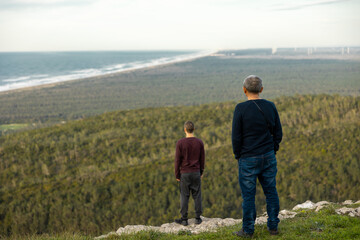 Father and son standing on top of mountain, staring at beautiful nature landscape. Forest and ocean background. copyspace. 