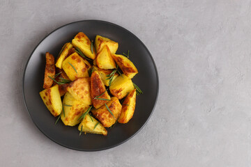 Fried potatoes on a black plate with spices and rosemary on a gray background with a copy space. Baked potatoes. Top view