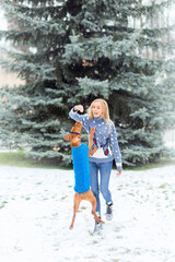 girl has fun playing with her dog in winter . A girl in a Christmas sweater trains a dog in a sweater.