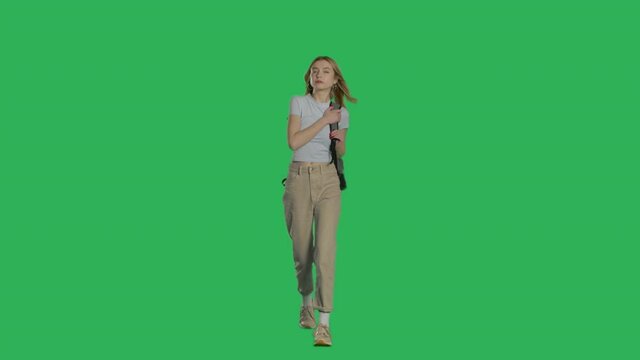Tired young woman walking with backpack on a Green Screen, Chroma Key. 4k UHD front view isolated video.