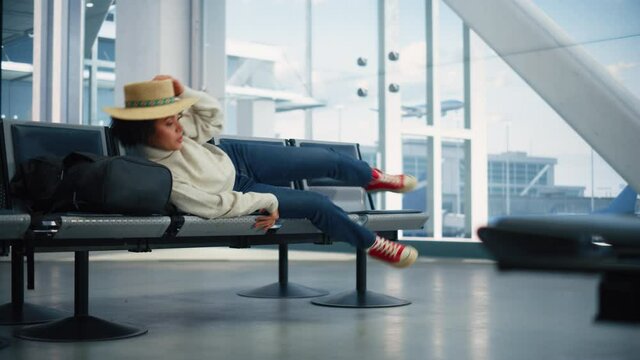 Airport Terminal: Beautiful Black Woman Lying Down for a Rest and Sleep while Waiting for Vacation Flight. Young and Happy Traveling Female Sleeps on the Seats of Boarding Lounge Airline Hub