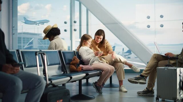 Busy Airport Airplane Terminal: Happy Beautiful Mother and Cute Little Daughter Wait for their Vacation Flight, Use Mobile Smartphone for Fun. Diverse Group of People in Boarding Lounge of Airline Hub