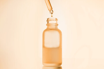face serum oil drop with dropper glass bottle pipette on yellow background close up