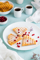 Heart shaped Belgian waffles with red berry and powdered sugar on a plate on the breakfast table. Valentine's Day. Vertical view