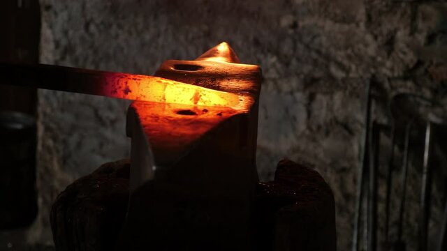 Panning motion of two blacksmiths hammering on an anvil forging a red-hot iron rod.