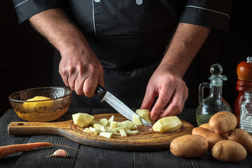 Before preparing the national dish, the chef cuts raw potatoes into small pieces with a knife. Close-up of a cook hands while working in a restaurant kitchen