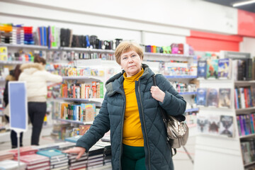  Mature woman in winter clothes among   bookshelves in   store