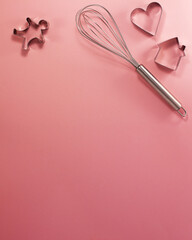 Steel whisk house men and heart shaped cutter at the top flat lay top view. Confectionery cooking concept with copy space on bright pink paper background
