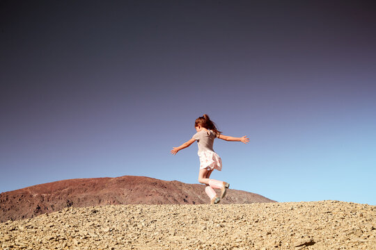 A girl spins around wearing a dress and cowboy boots in the desert
