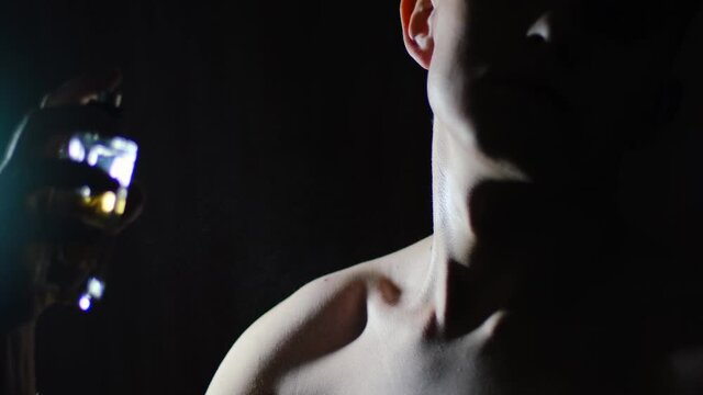 Young man applying perfume to skin in the dark