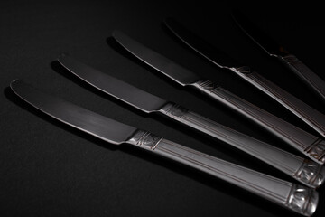 Knives made of metal, silver, lie on a black background with a glare of light