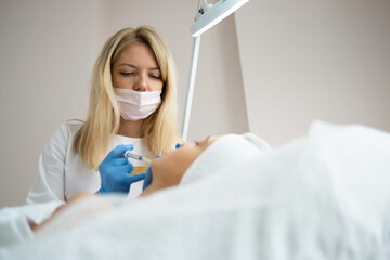 Female doctor injecting hyaluronic acid into the chin of a woman as a facial rejuvenation treatment