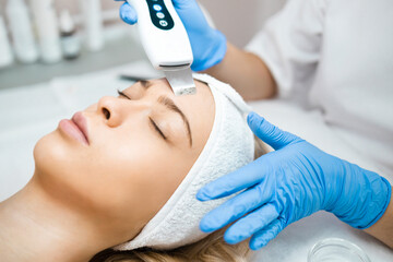 Professional skin care. Cosmetologist in blue gloves does ultrasound cleaning of a woman's face...