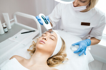 Obraz na płótnie Canvas Cosmetologist or dermatologist making ultrasound facial cleaning for woman in beauty salon. Skin care procedure
