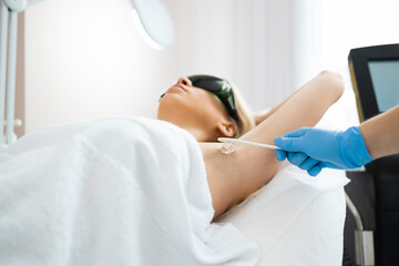 Applying hair removal gel under the arms. Woman at a laser epilation session with a modern laser in...
