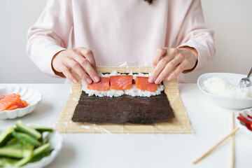 Sushi preparation process, the girl makes sushi with different flavors - fresh salmon, caviar, avocado, cucumber, ginger, rice.