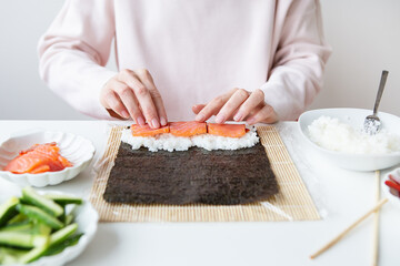 Sushi preparation process, the girl makes sushi with different flavors - fresh salmon, caviar, avocado, cucumber, ginger, rice.
