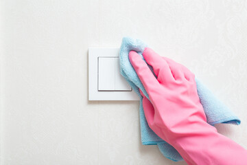 Cleaner hand in pink rubber protective glove holding blue dry rag and wiping white plastic light...