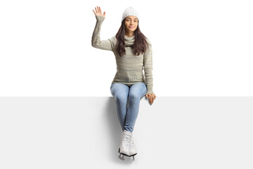 Casual young female with ice skates sitting on a blank panel and waving