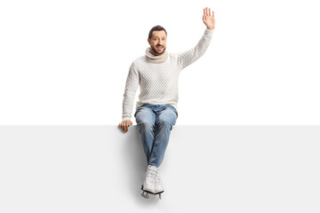 Casual young man with ice skates sitting on a blank panel and waving
