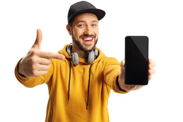Casual modern guy with headphones and a cap holding a smartphone and in front of camera