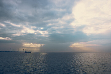 Obraz na płótnie Canvas Wind turbine - the sky and the sea, the sun breaks through the clouds, cargo ship at sea