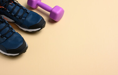 pair of blue sneakers and purple dumbbells on a beige background, sports. Copy space