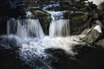 In the heart of the mountains in winter, at night, a river, the water falling on the foamy rocks and the snow on each side