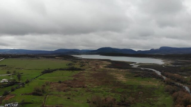 Village on plateau on cloudy sky landscape from landing flying drone. Aerial view of lake in the foothills. Mountain peaks in the background on fogy sky.