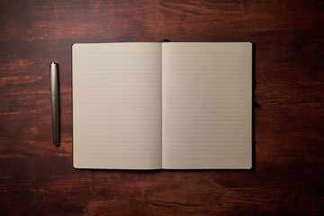 Notepad laying on a wood desk with a ballpoint pen. Evening mood through the desk light. Open...