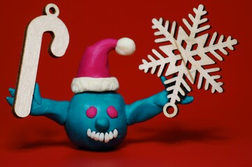 A figure of a virus in a New Year's hat with ornaments in his hand on a red background.