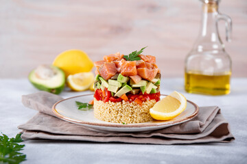 Salmon tartare with tomatoes, avocado and quinoa on a plate and light gray table