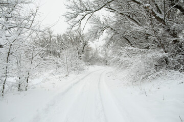 Winter road snowfall. An empty rural road without cars, covered with snowdrifts. Travel in bad weather. Winter cloudy landscape with a country road. Tracks of passing cars. The concept of winter magic