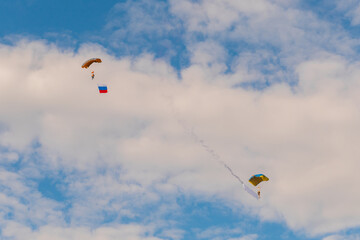 Two skydivers, parachutists flying with parachute against blue sky with white clouds at Air Show....