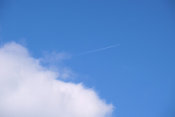 Distant passenger jet plane flying on high altitude on blue sky with white clouds leaving smoke trace of contrail behind. Air traveling concept