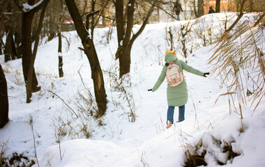 Kiev, Ukraine, January 2, 2022. Schoolgirl in warm green down jacket walks along snow-covered path in winter park, forest, woodland. Woman, teen girl in warm coat with backpack on street at frosty day